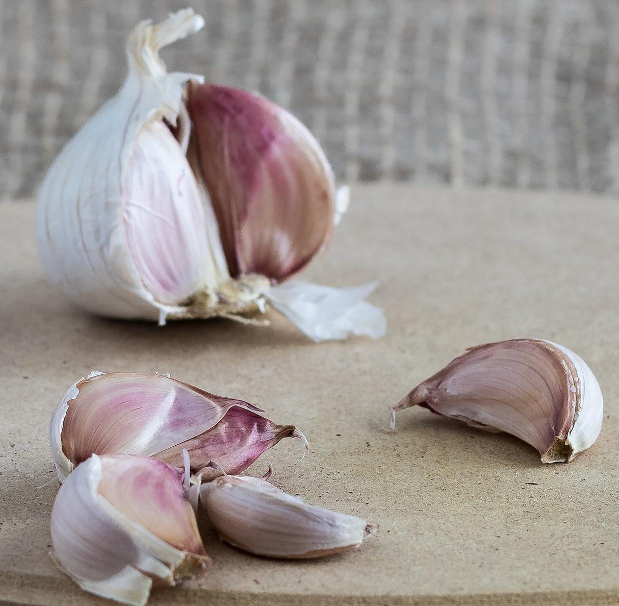 one bulb of garlic with red skin and several cloves broken out of the bulb laying on a table in front of it